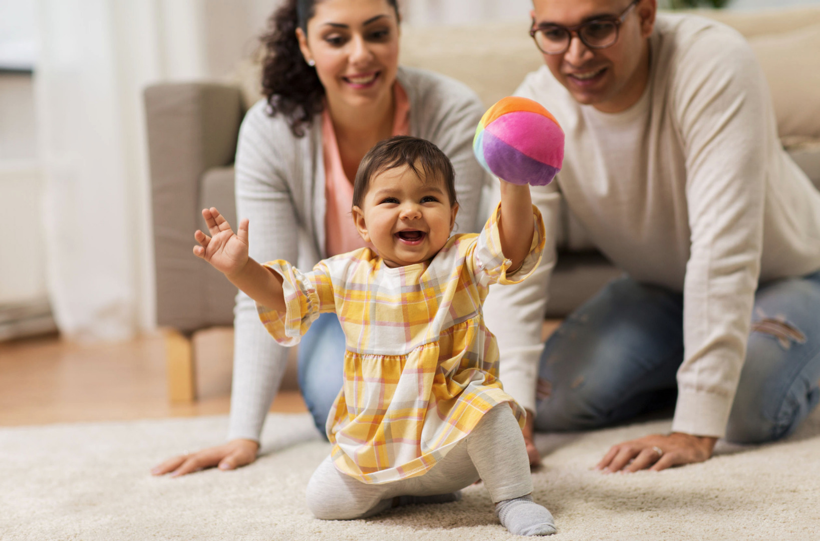 toddler holding up ball with parents