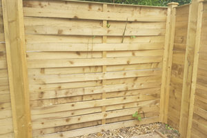 Woven Panels pressure treated horizontal wooden boards, divided by a wood baton separating the neighbouring board in the centre of the panel allowing wind to pass through within a baton frame