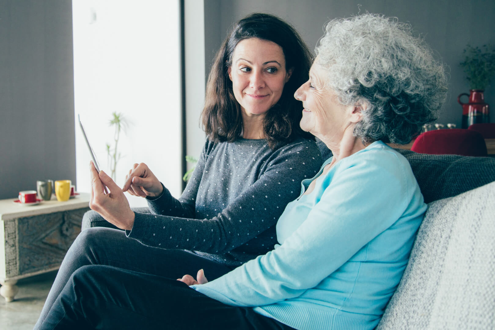 Carer and senior woman smiling while using a tablet