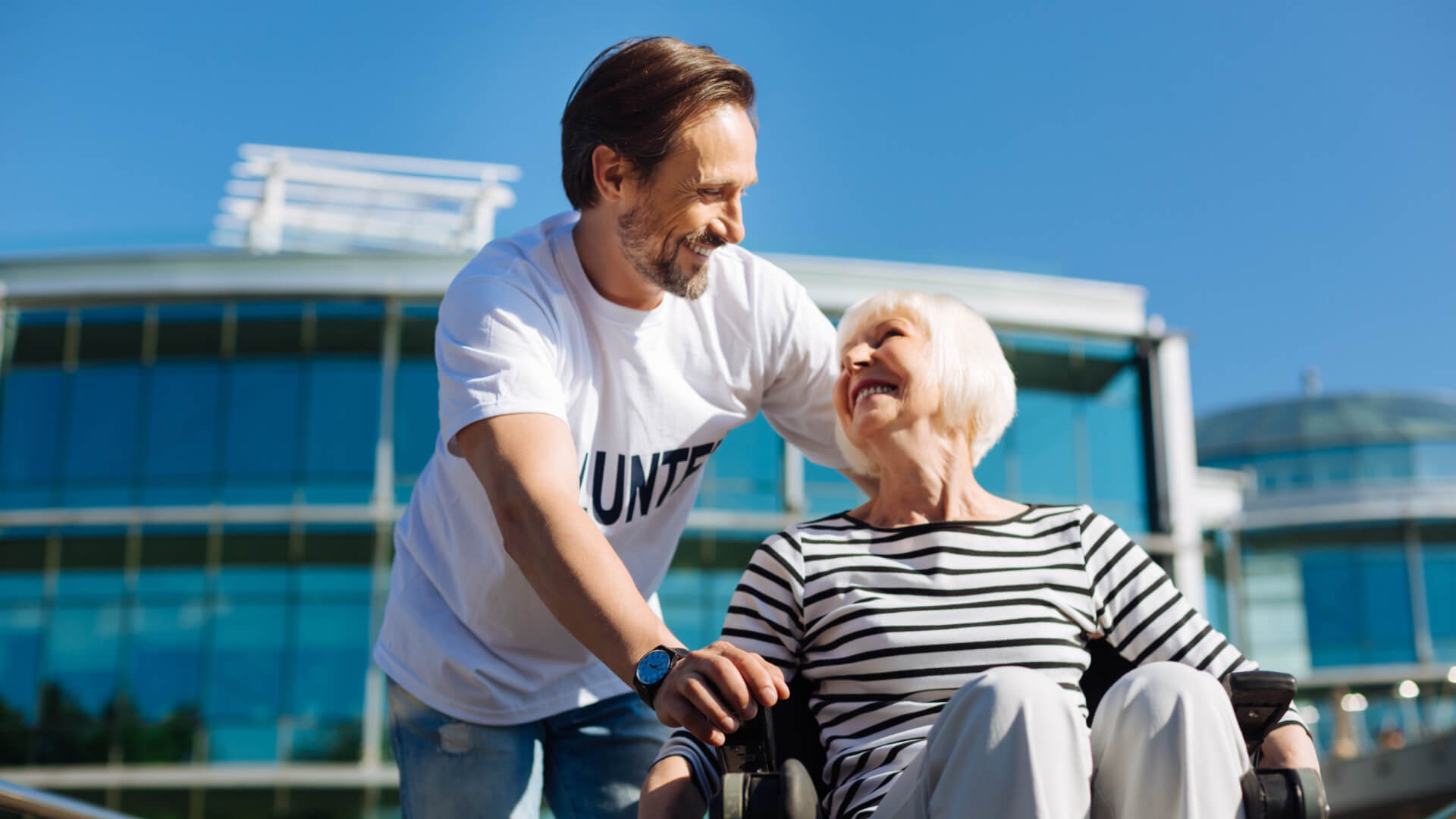 Volunteer carer walking woman in wheelchair on a sunny day