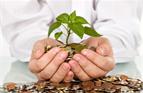 Businessman holding plant sprouting from a handful of coins - good investment and money concept